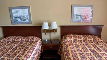 Een hotelkamer met twee bedden, elk voorzien van een beddekleed met dessin, een nachtkastje met twee lampen en twee ingelijste foto’s aan de muur.