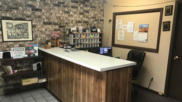A reception area with a wooden counter, a brick wall, a computer, and a calendar. - Budget Host Village Inn (Kirksville)