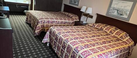 Habitación de hotel con dos camas, un escritorio, una silla, un lavamanos y un espejo.