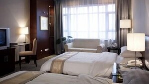 Een hotelkamer met twee bedden, een bureau, een stoel, een televisie en een raam met gordijnen.