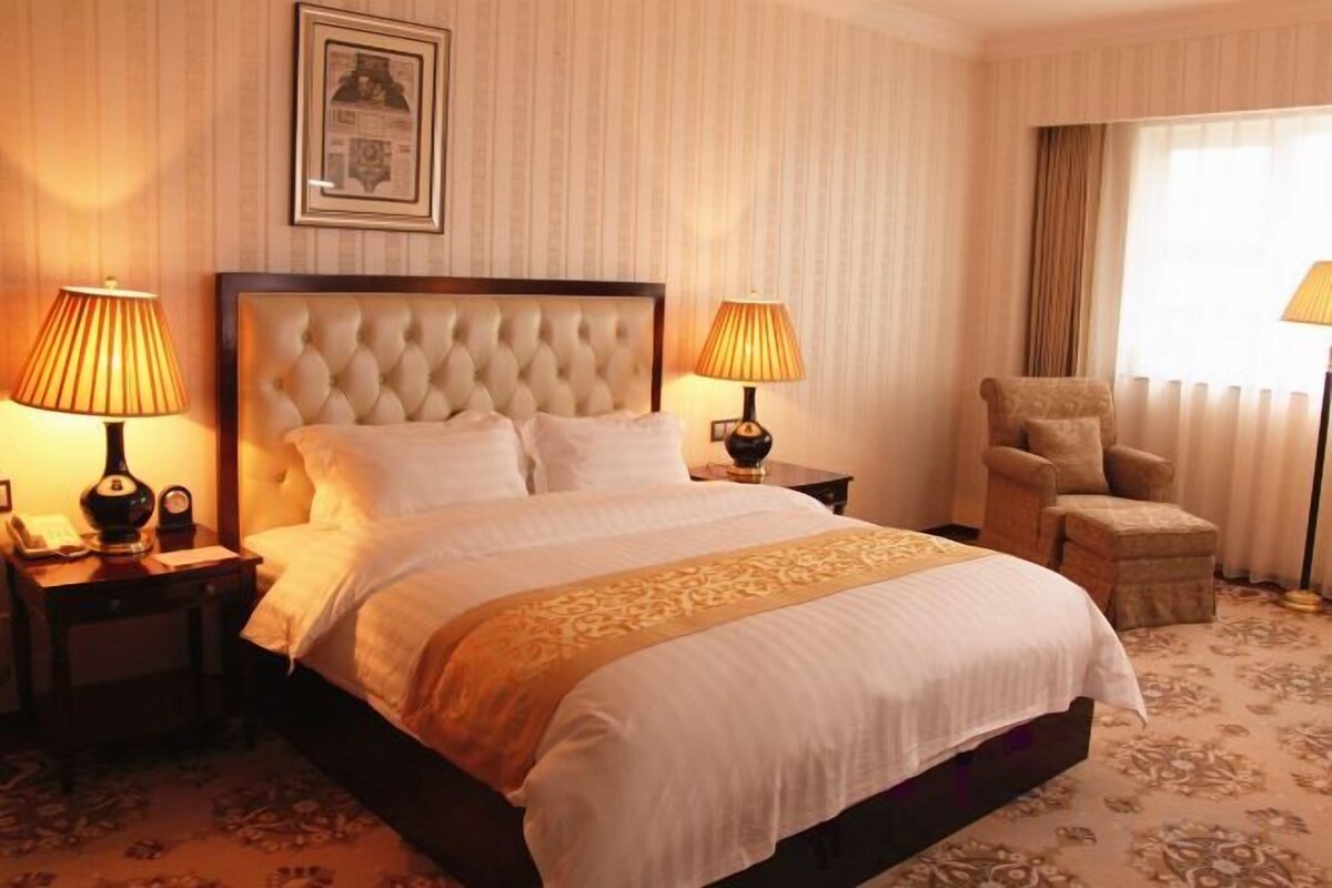 A hotel room with a large bed, two bedside tables with lamps, a chair, and a window with curtains.