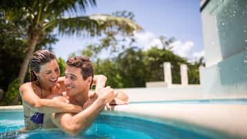 A couple in a swimming pool with a clear view of the pool's edge and surrounding palm trees.