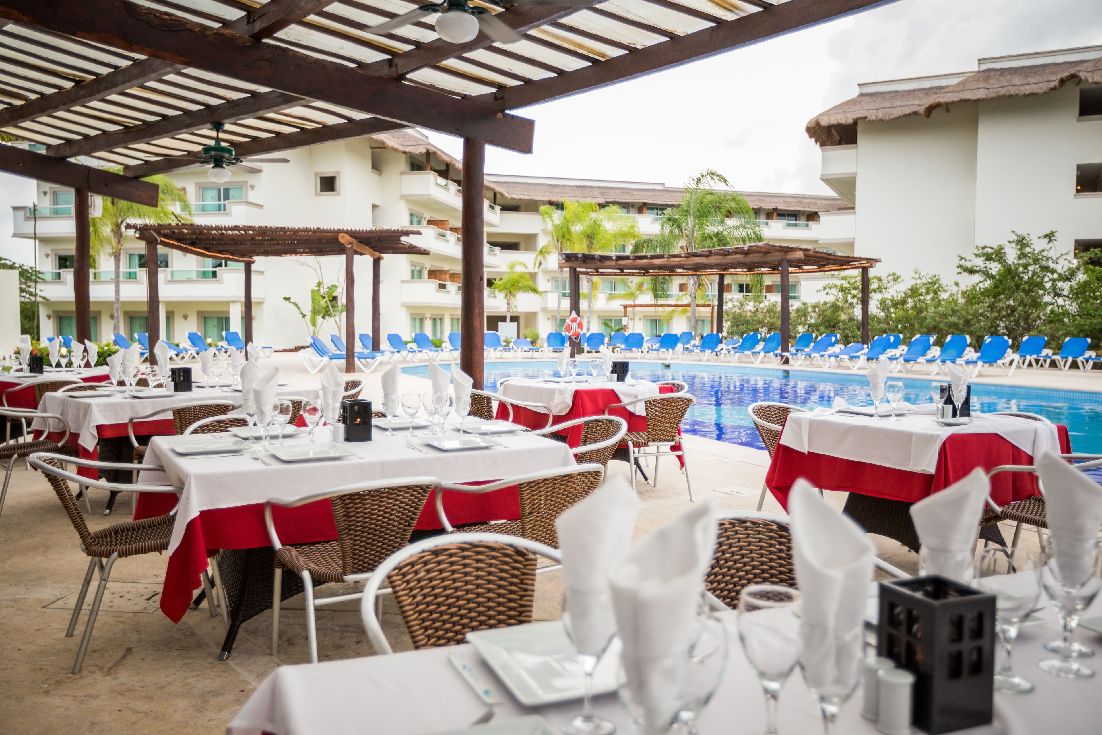 A poolside restaurant with tables set for dining, overlooking a swimming pool.