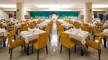 Un gran comedor con varias mesas y sillas, un escenario con una pantalla grande y un telón de fondo verde.