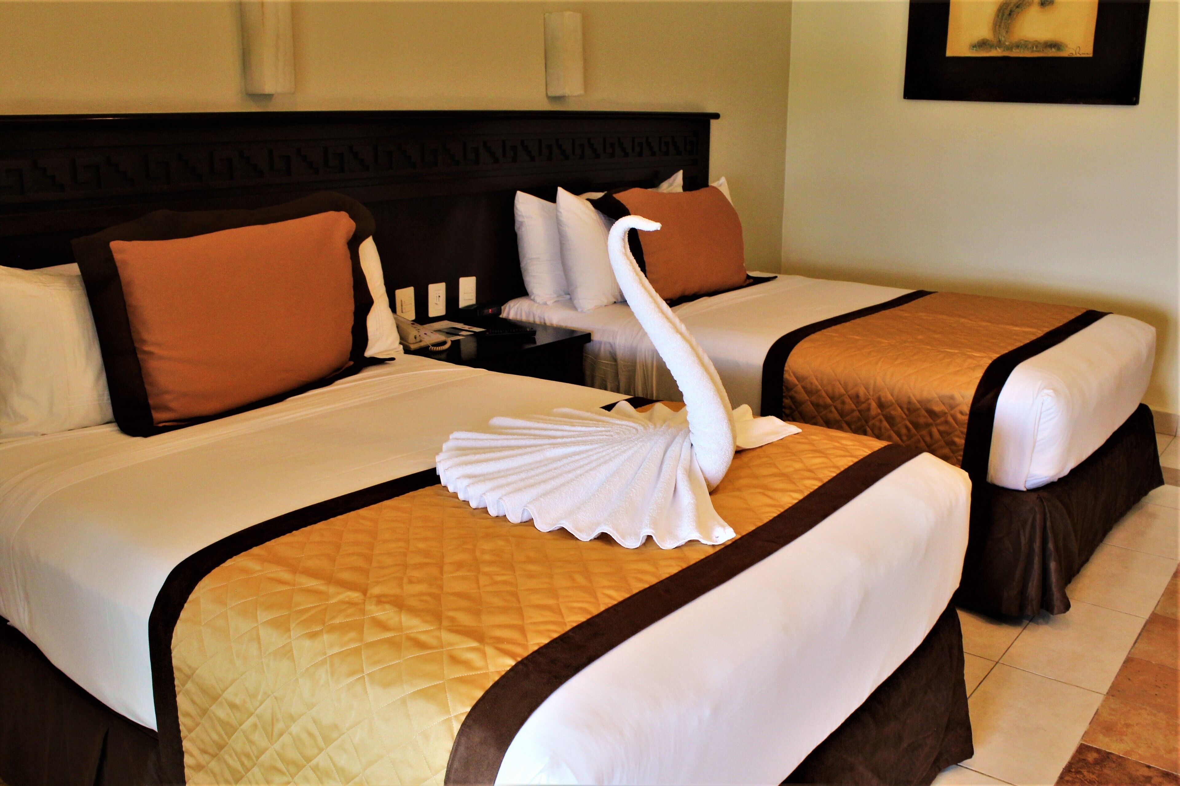 A hotel room with two beds, each with a brown headboard, white bedding, and a decorative swan towel.
