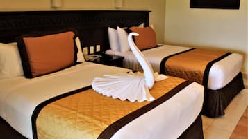 Habitación de hotel con dos camas, cada una con cabecera marrón, ropa de cama blanca y una toalla decorativa con forma de cisne.