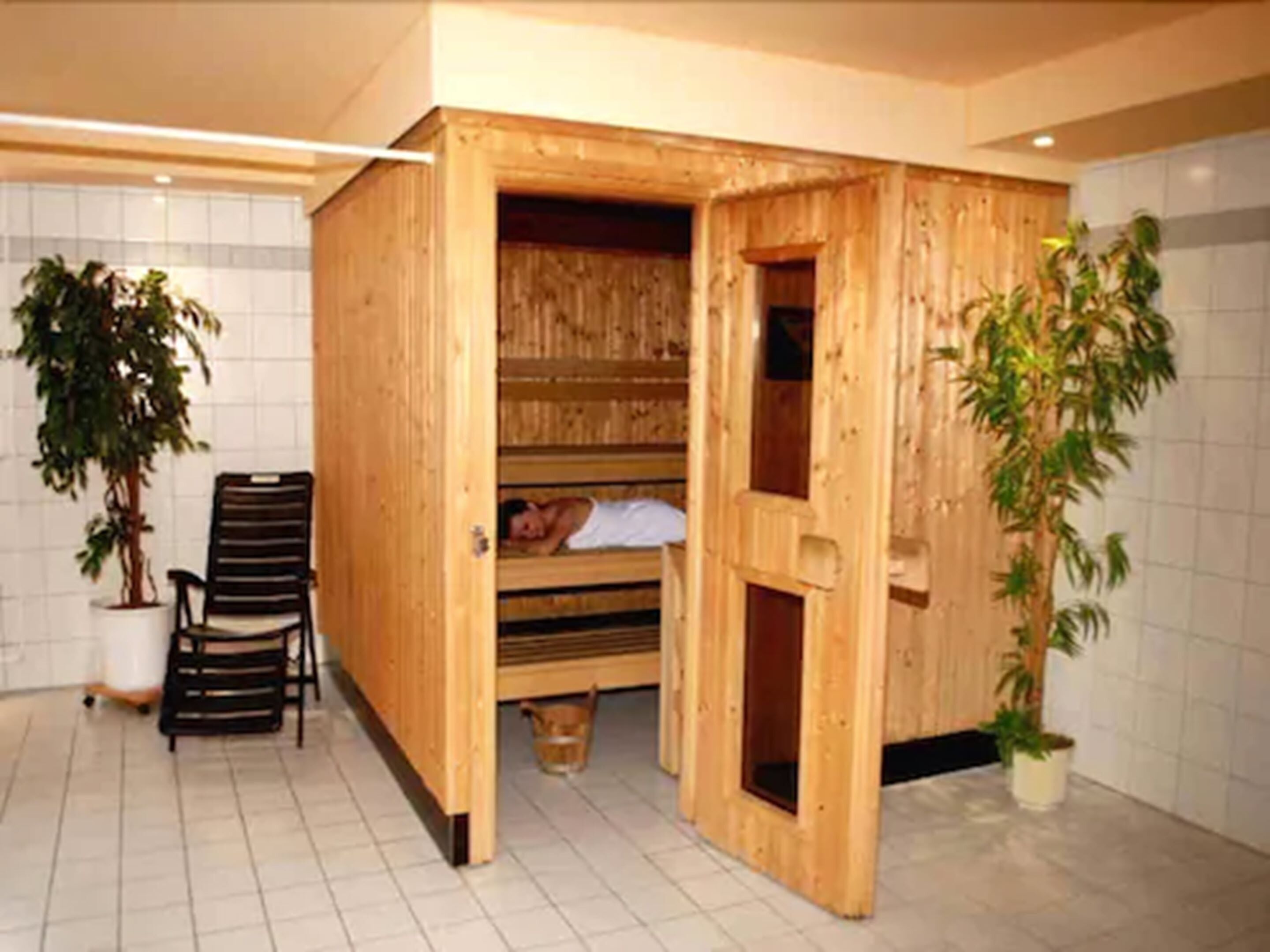 Een houten sauna met een bank en een zitbank, omringd door potplanten.
