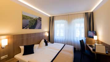 A hotel room with a bed, a desk with a computer, a television, and a painting on the wall.