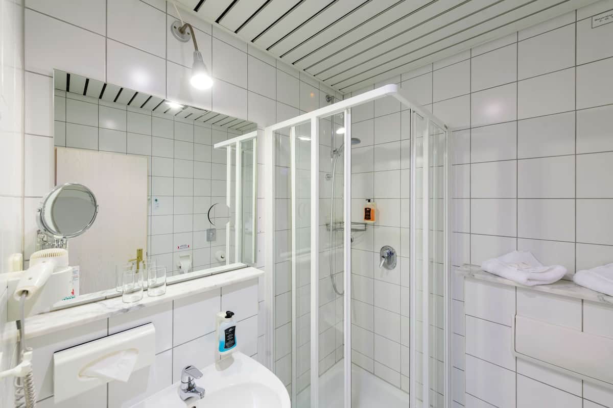 A modern bathroom with a glass-enclosed shower, a large mirror, and a white sink.