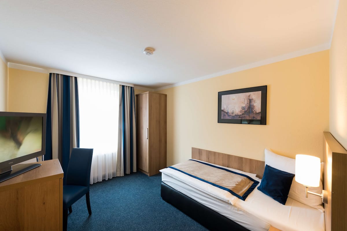A hotel room with a bed, a desk with a television, a chair, and a painting on the wall.