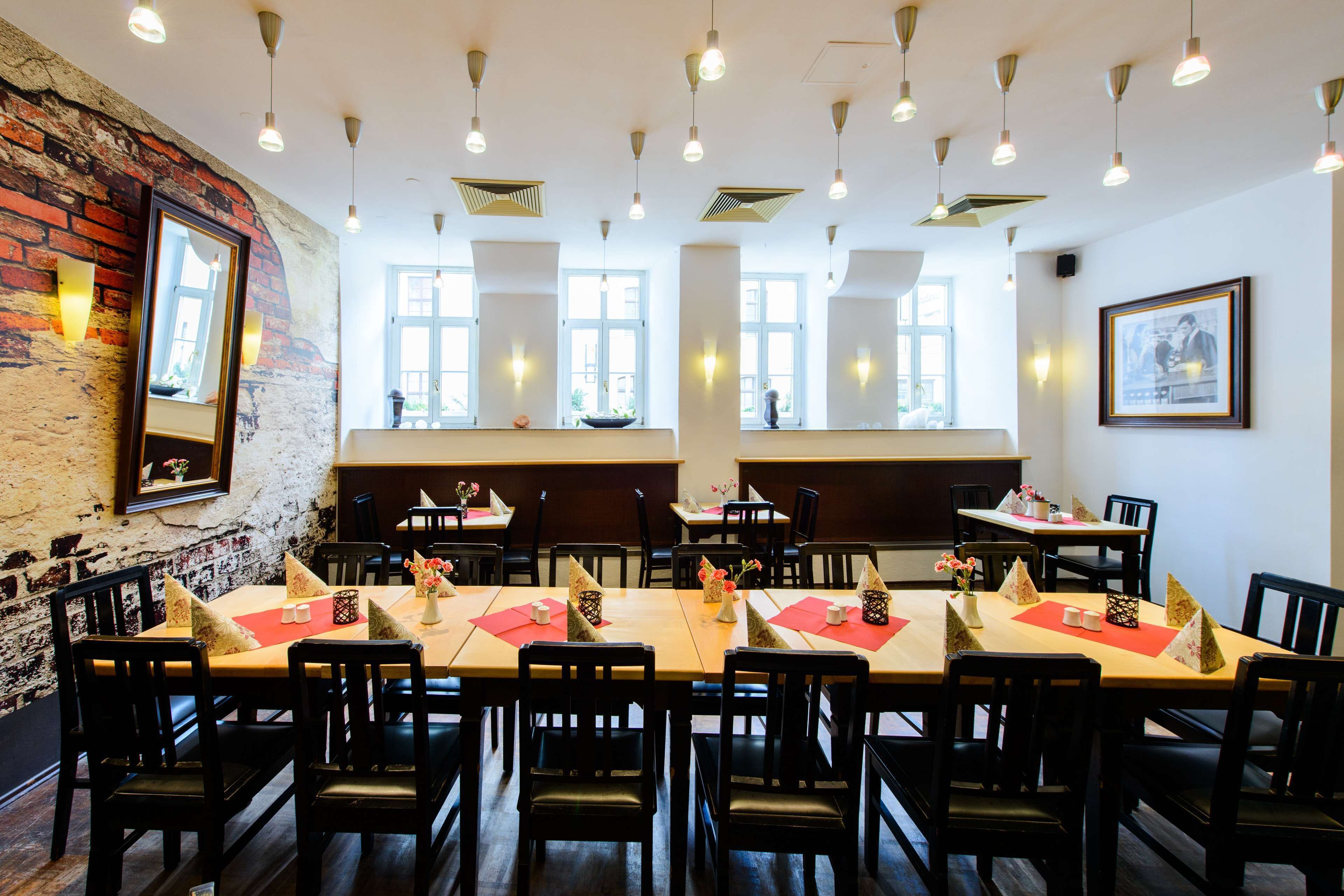 Un restaurante con varias mesas, cada una con individuales rojos y velas, y una pared de ladrillo en un lateral.