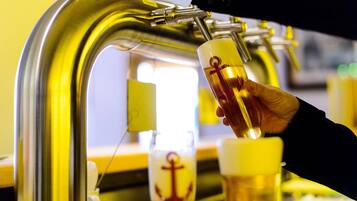 En hånd skænker øl fra et fad i et glas med et ankerlogo.