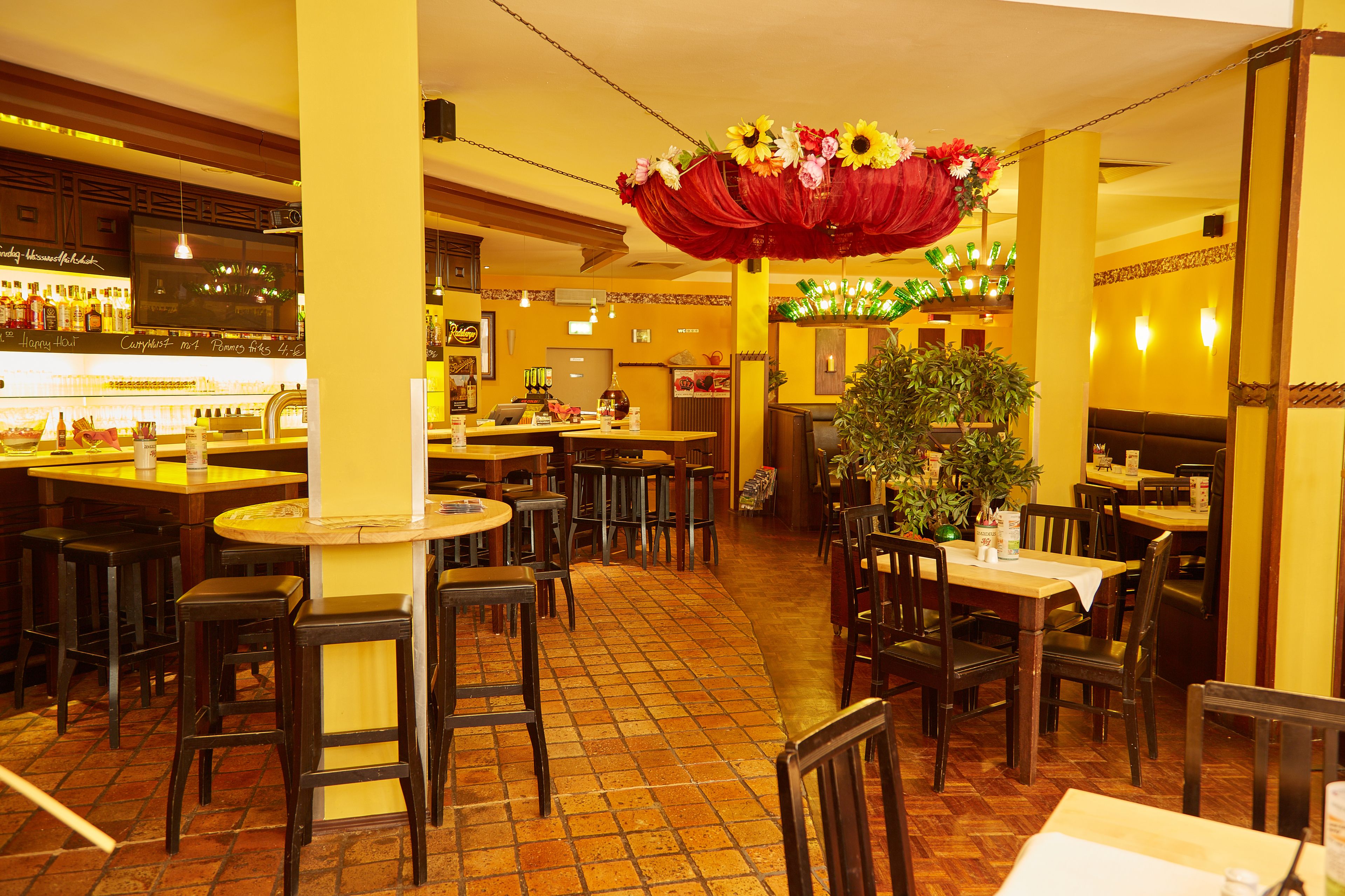 Un interior de restaurante con varias mesas y sillas, una zona de bar y un arreglo floral decorativo.