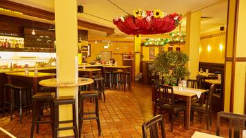 Un interior de restaurante con varias mesas y sillas, una zona de bar y un arreglo floral decorativo.