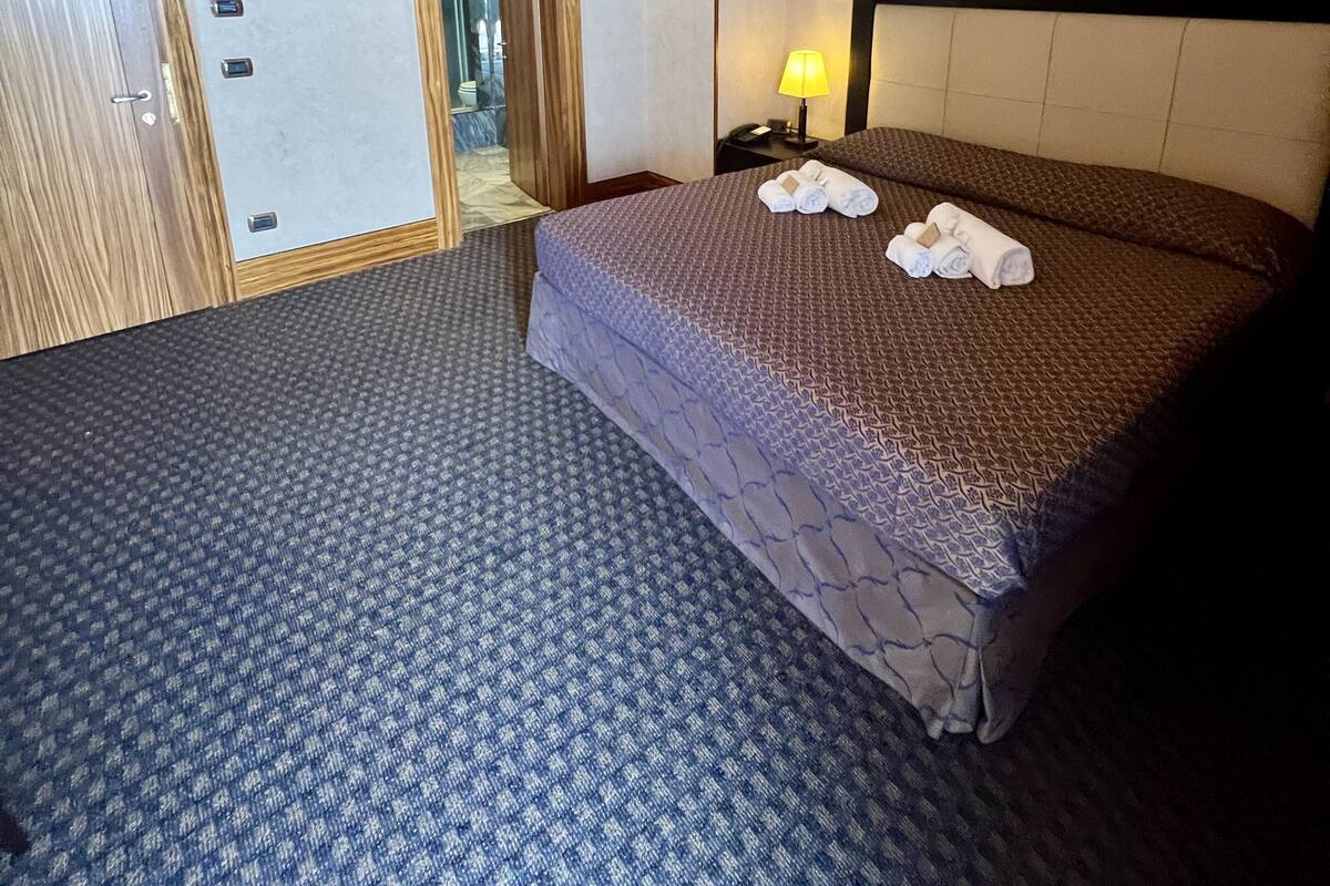 Une chambre d’hôtel avec un grand lit, une table de chevet avec une lampe, un miroir et une porte avec une poignée.