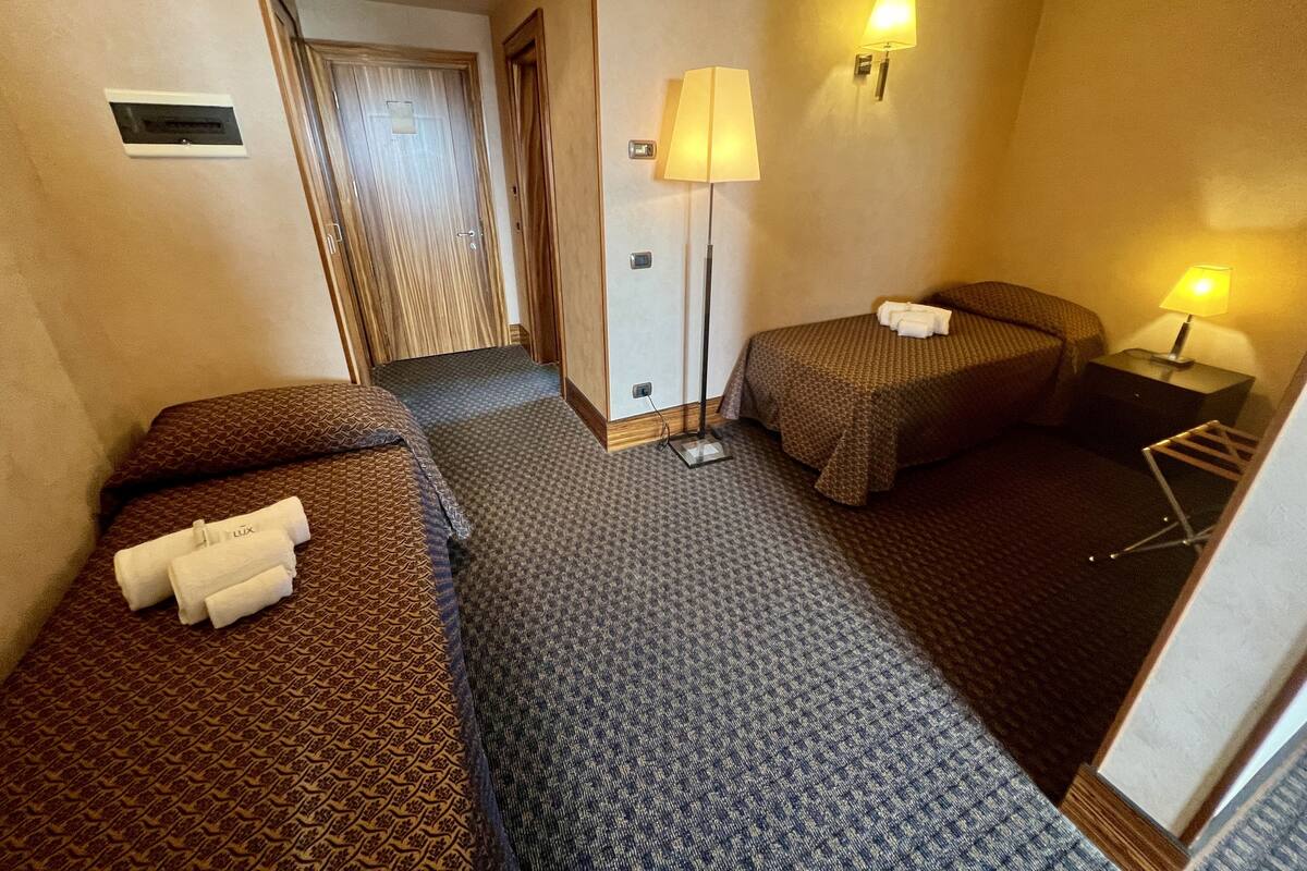 Une chambre d’hôtel avec deux lits, une table de chevet, une lampe et une porte donnant sur une autre pièce.