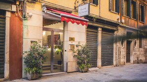 A building with a storefront, potted plants, and a red awning. - Locanda Ca' Lucrezia (Venice)