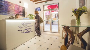 A reception desk with a sign reading 'Locanda Ca' Luceria,' a glass table with a vase of flowers, and a wooden chair. - Locanda Ca' Lucrezia (Venice)