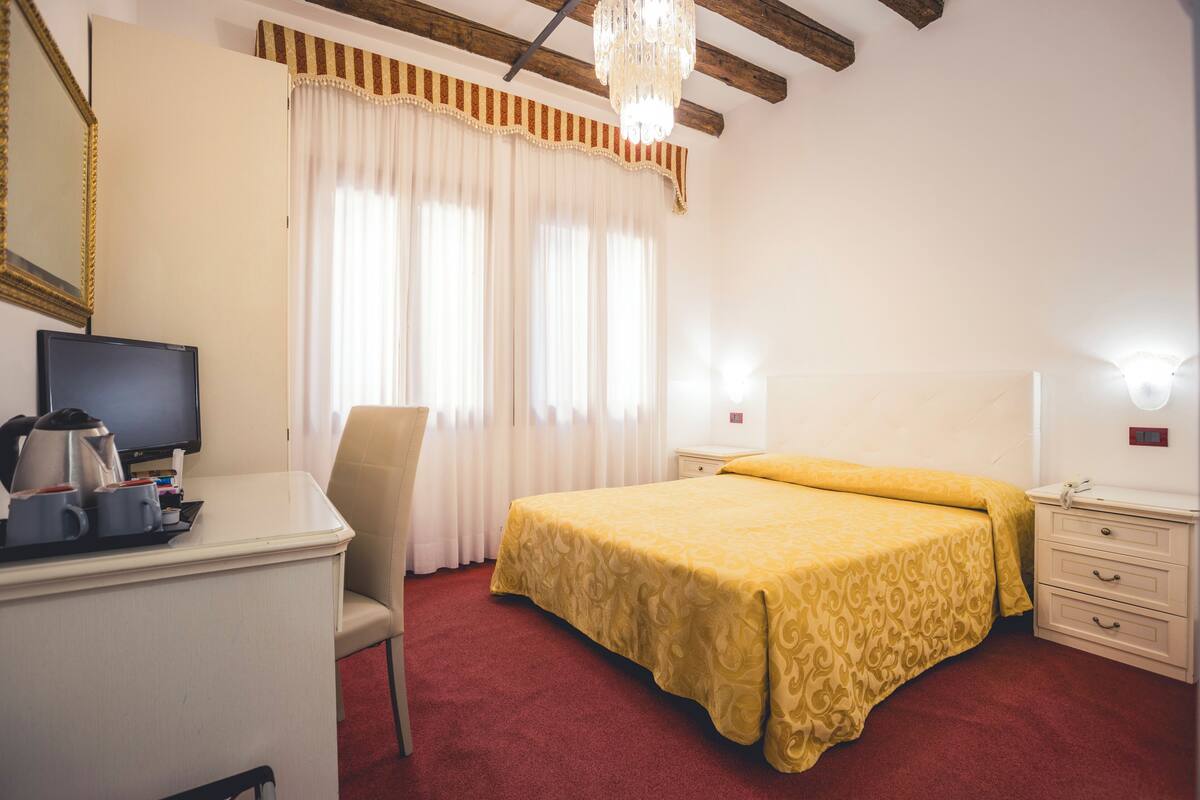 A hotel room with a bed, a desk with a television, a chair, and a nightstand.