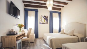 A hotel room with a bed, a desk, a chair, a TV, and a chandelier. - Locanda Ca' Lucrezia (Venice)