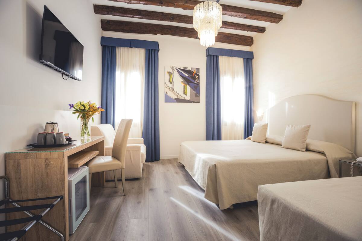 A hotel room with a bed, a desk, a chair, a TV, and a chandelier.