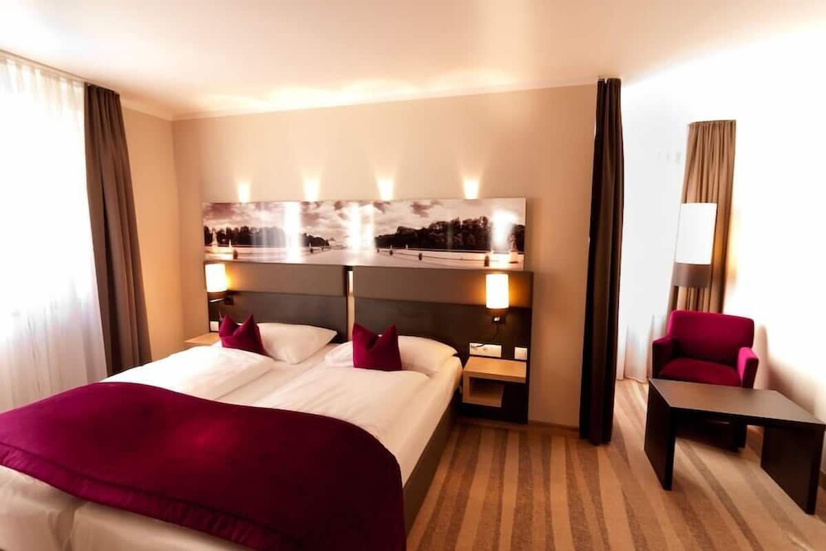 Ein Hotelzimmer mit einem großen Bett, einem Schreibtisch, einem Stuhl und einem an der Wand befestigten Fernseher.