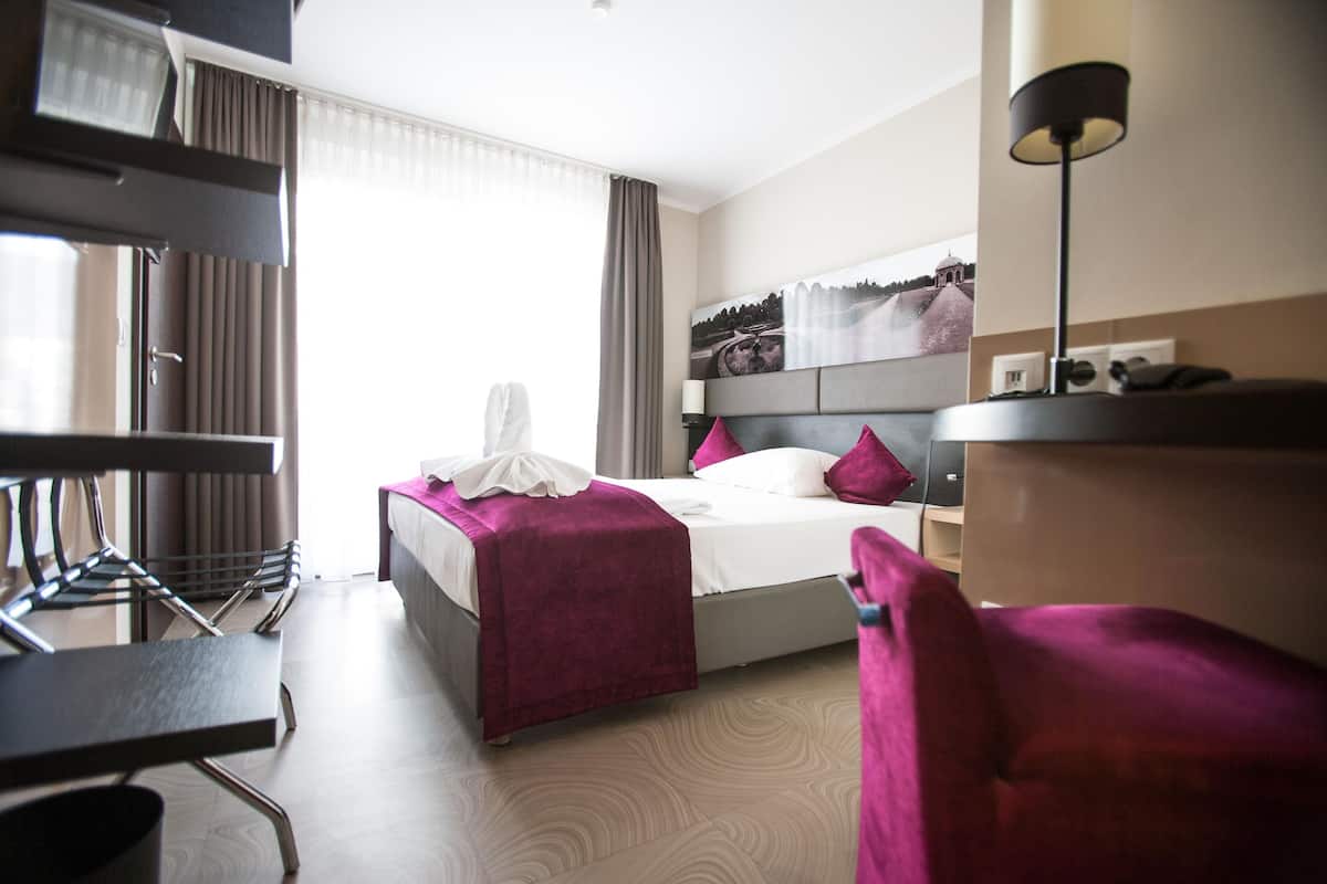 Ein Hotelzimmer mit Bett, Schreibtisch, Stuhl und einem Vorhangfenster.