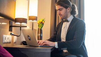 A man in a suit working on a laptop at a desk with a vase of flowers and two wall-mounted lamps.