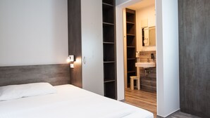 Quarto com cama, guarda-roupa e banheiro visível por uma porta aberta.