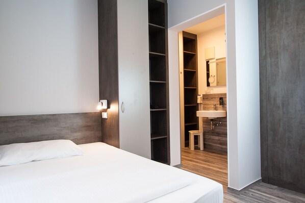 Une chambre à coucher avec un lit, une armoire et une salle de bain visible à travers une porte ouverte.