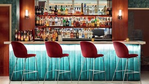 A bar area with multiple shelves of liquor bottles, a bar counter, and four red bar stools. - Manhattan Centre Hotel (New York)