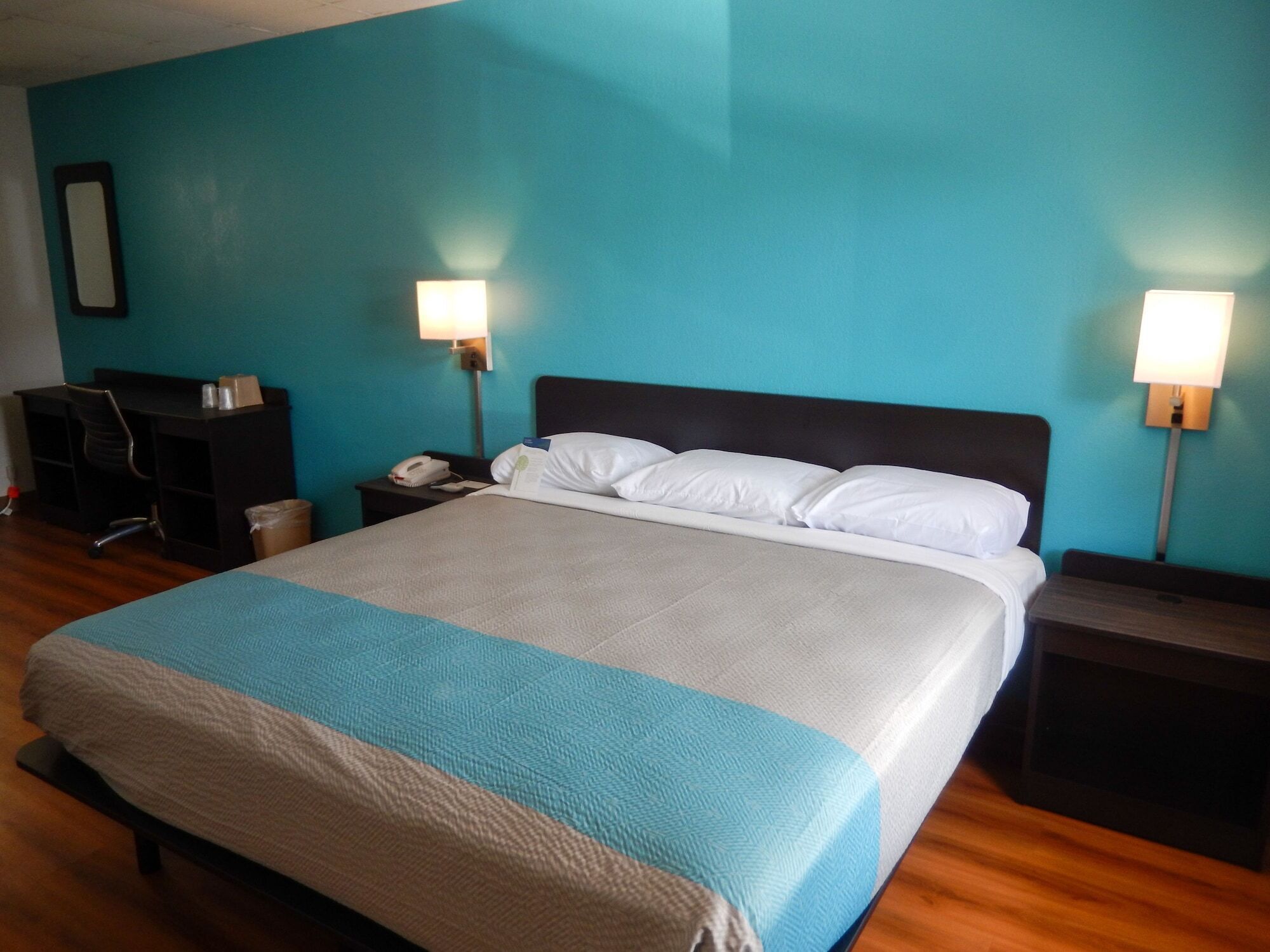 A hotel room with a bed, two bedside tables, a desk with a chair, and a trash bin.