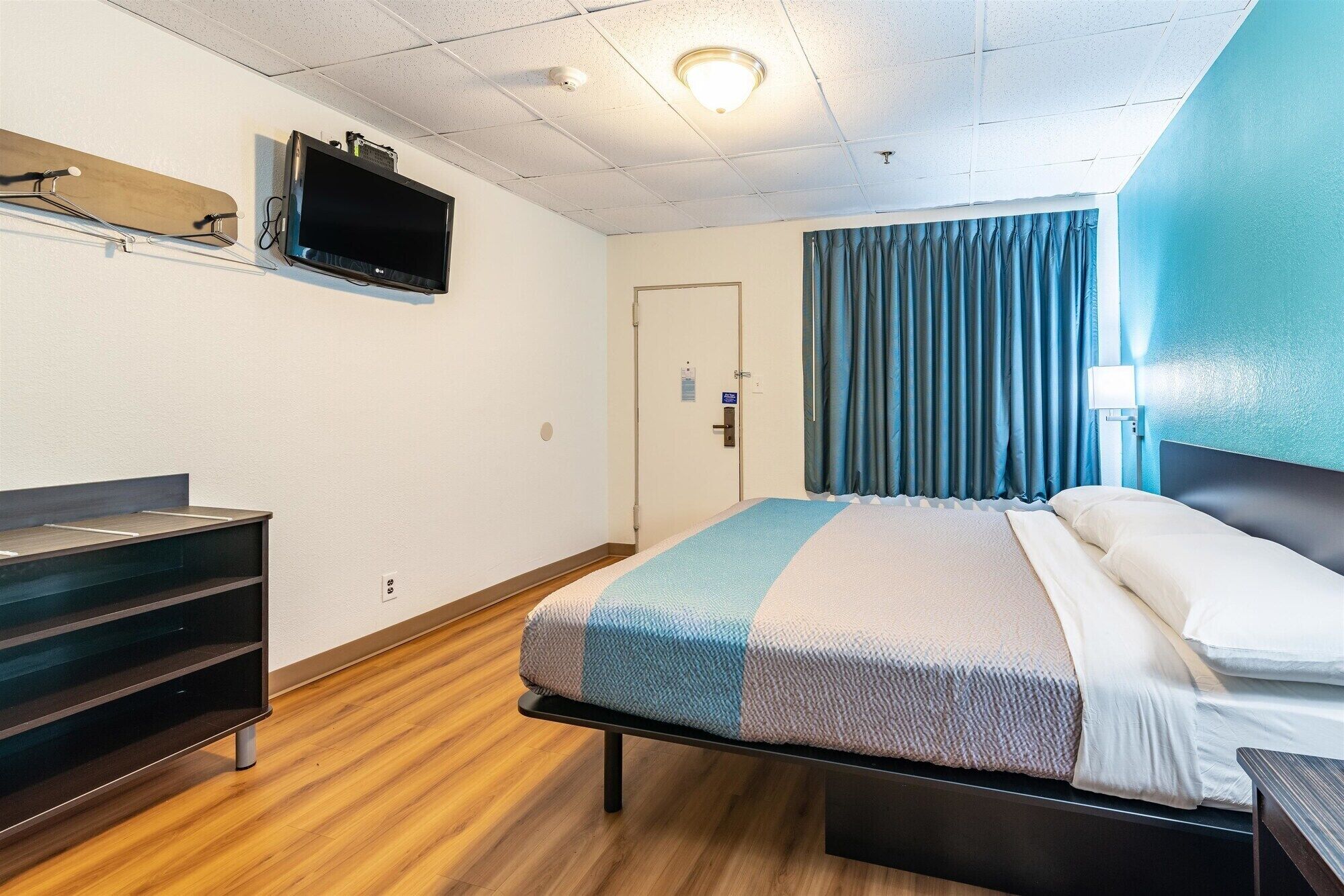 Une chambre d’hôtel avec un lit, un téléviseur fixé au mur, un bureau et une porte.