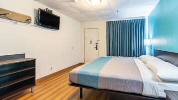 Une chambre d’hôtel avec un lit, un téléviseur fixé au mur, un bureau et une porte.