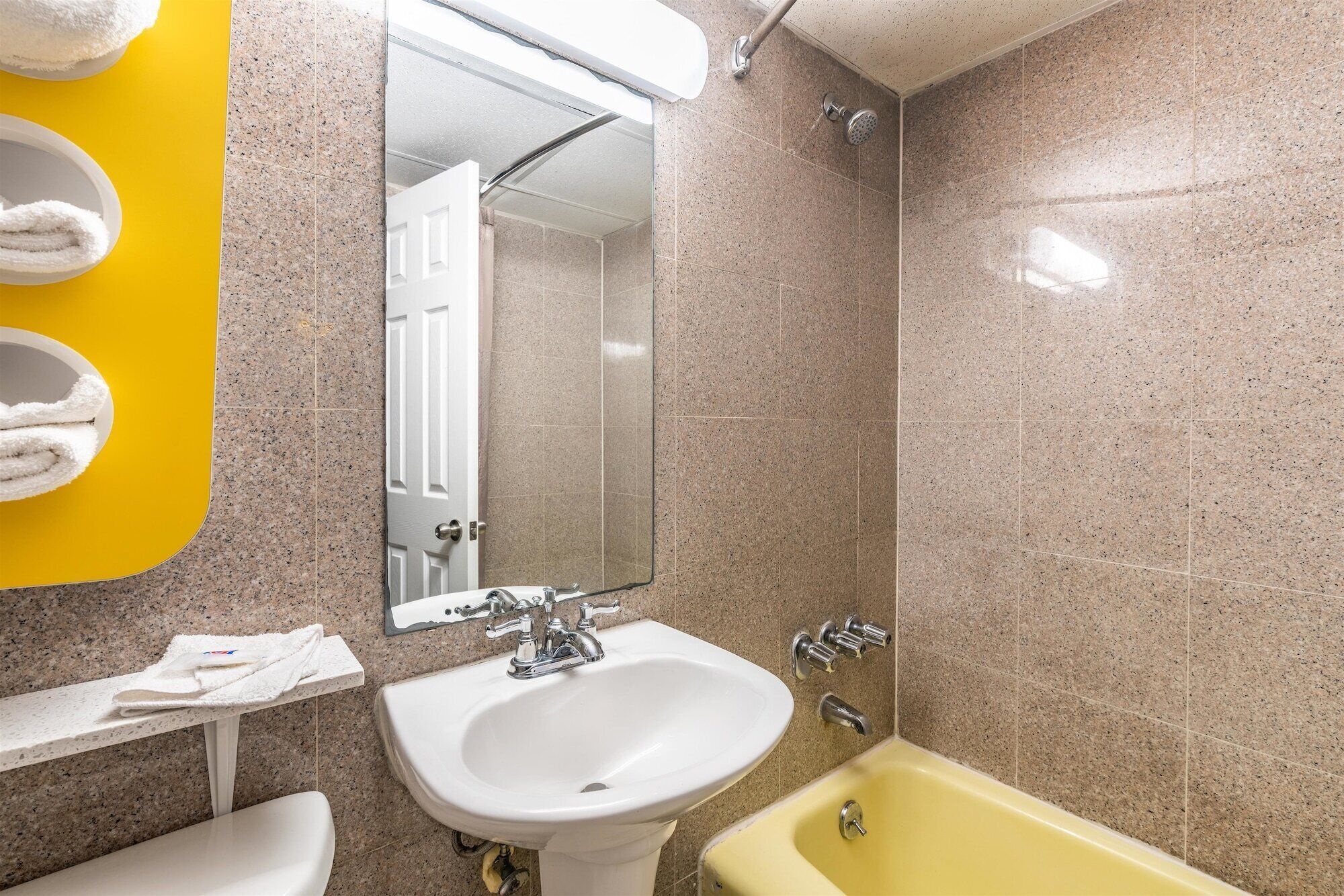 A bathroom with a sink, mirror, shower, and yellow bathtub.