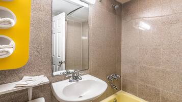 A bathroom with a sink, mirror, shower, and yellow bathtub.