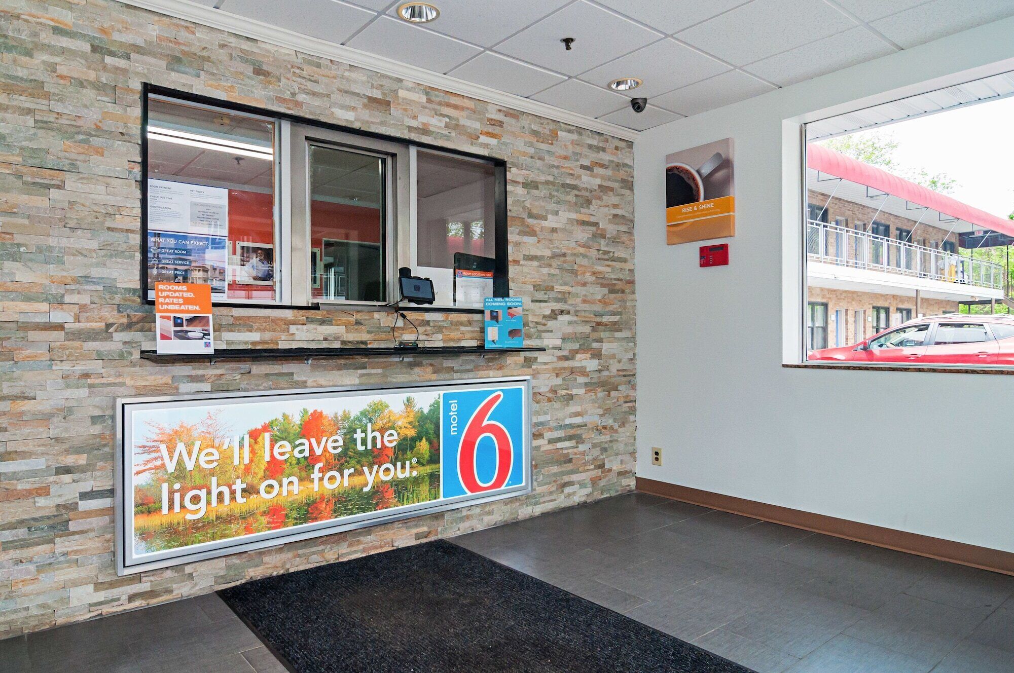 A motel lobby with a stone wall, a reception desk, a large billboard advertising the motel, and a view of the street outside.
