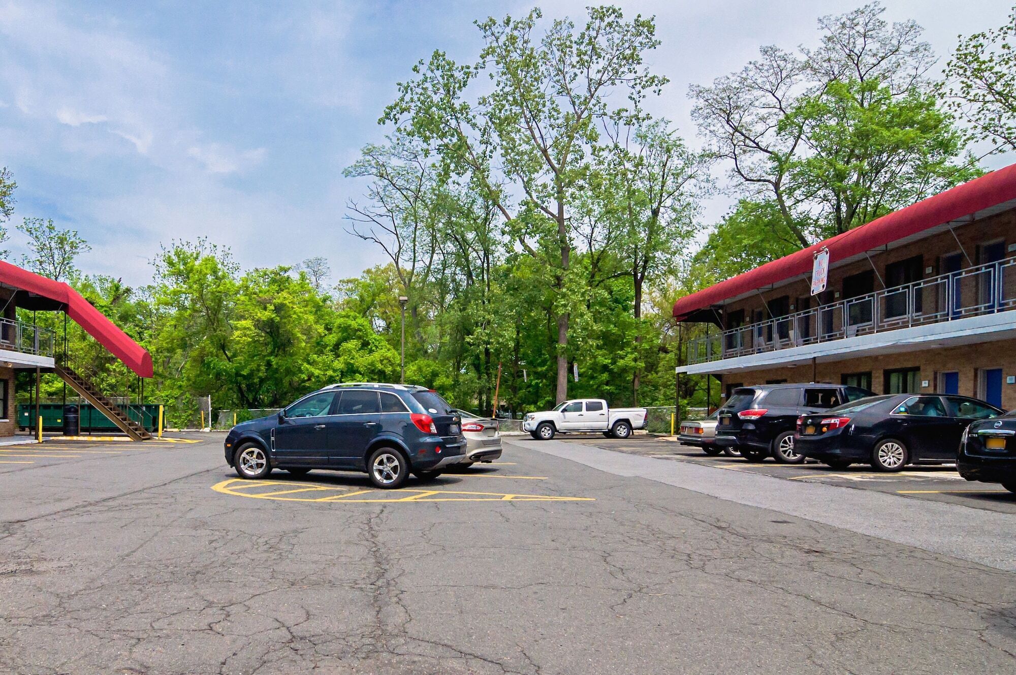A parking lot with several cars, a building with a red awning, and trees in the background.
