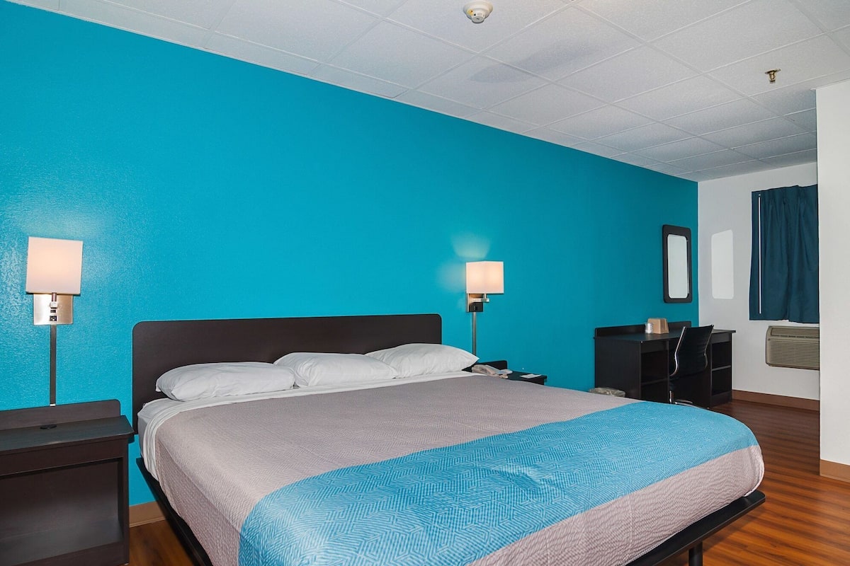 A hotel room with a large bed, two bedside lamps, a desk with a chair, a mirror, and a wardrobe.