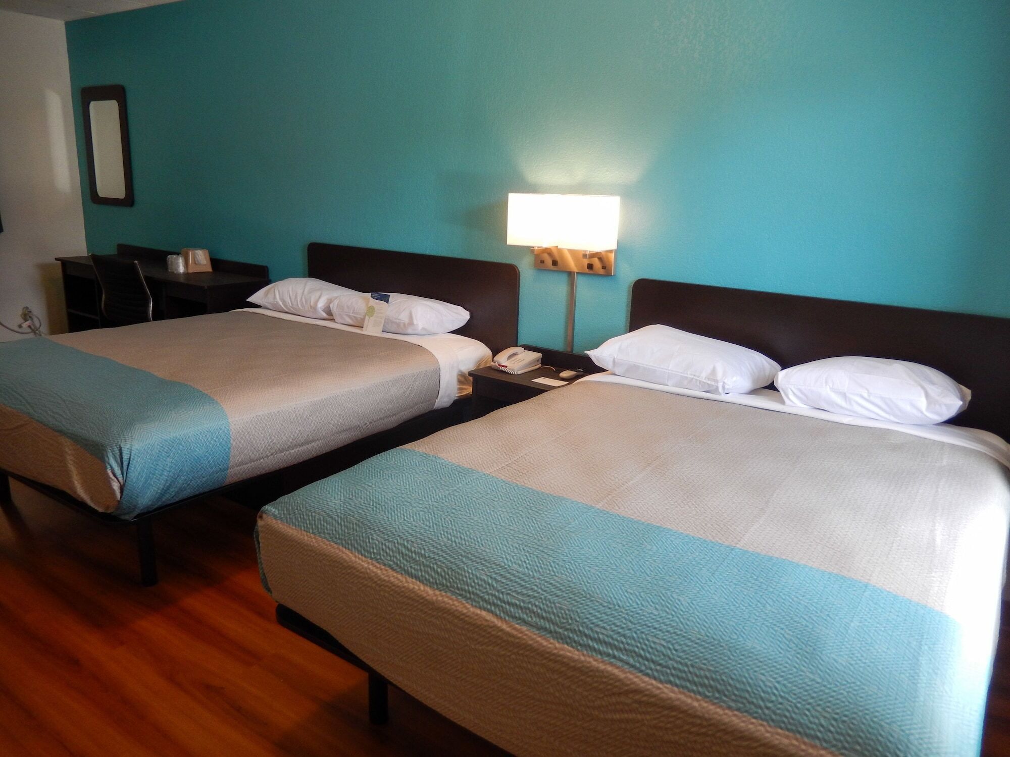 Quarto de hotel com duas camas, uma escrivaninha, uma cadeira, um abajur e uma mesa de cabeceira.
