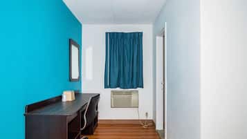 A small, narrow room with a desk, chair, and a window with blue curtains.