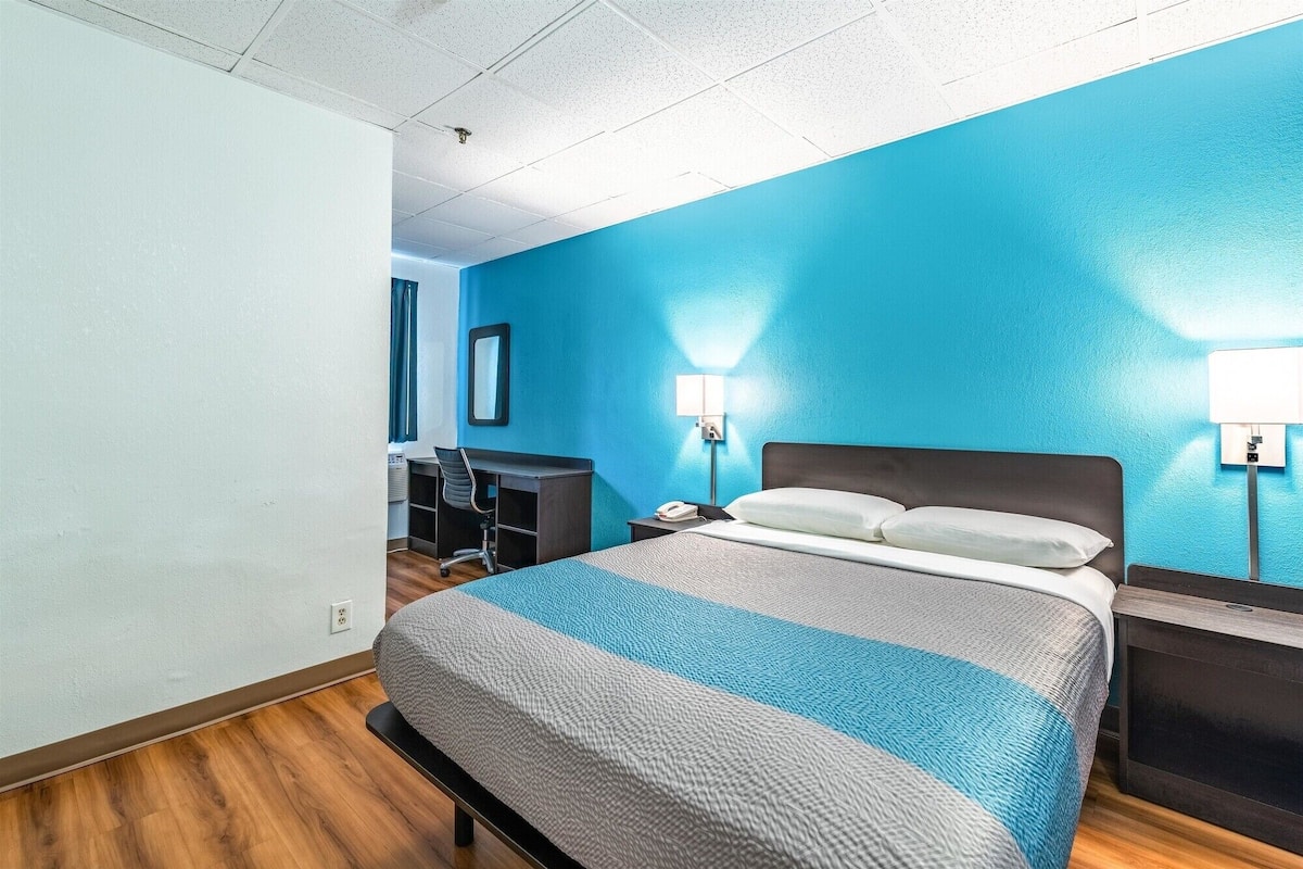 A hotel room with a bed, desk, chair, and two bedside lamps.