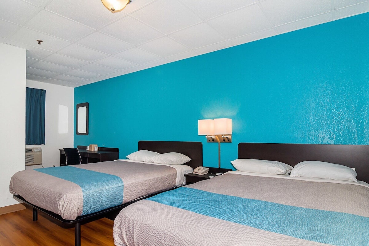 A hotel room with two beds, a desk, a chair, a lamp, and a window with curtains.