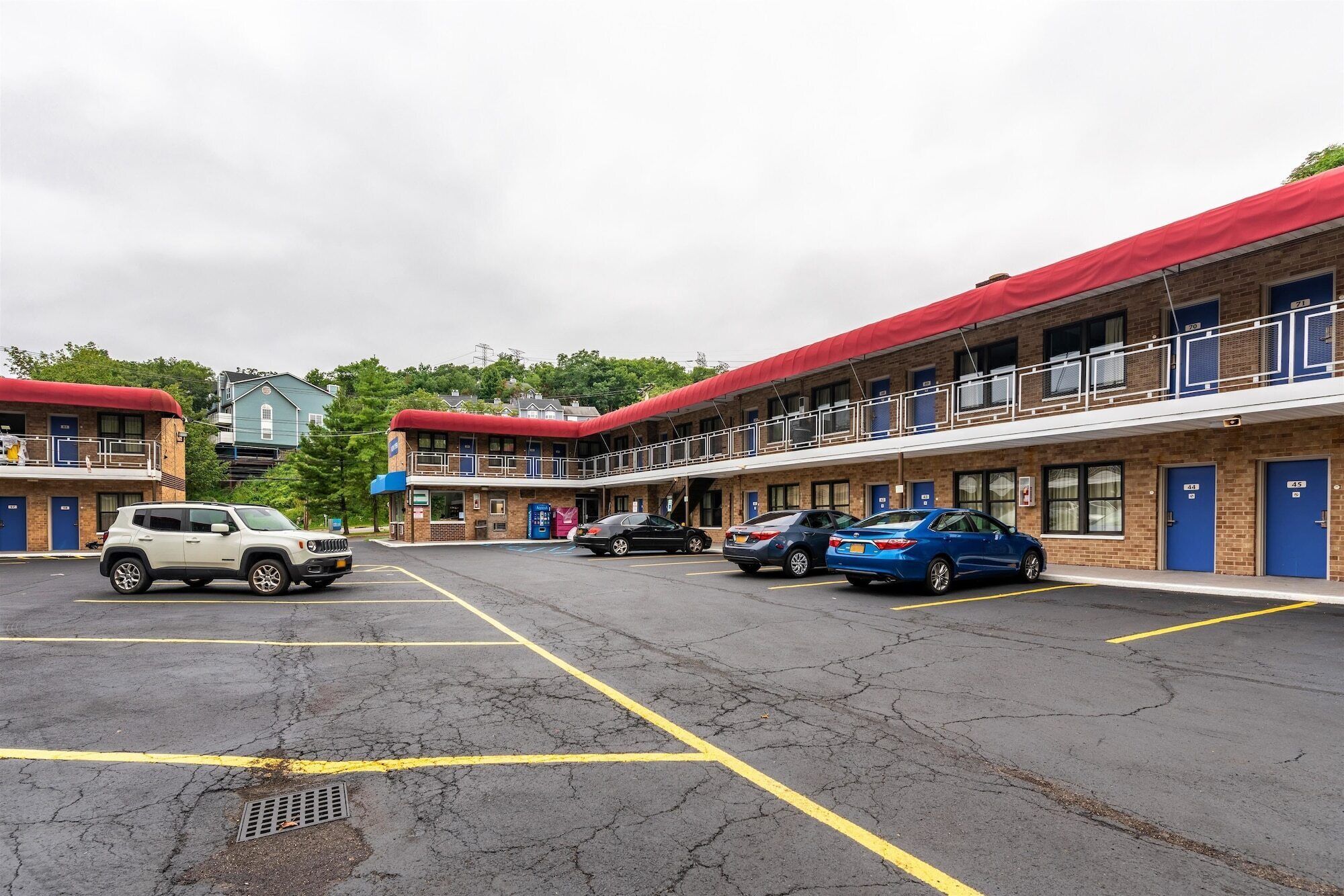 A motel with multiple rooms, a parking lot, and a building with a red roof.