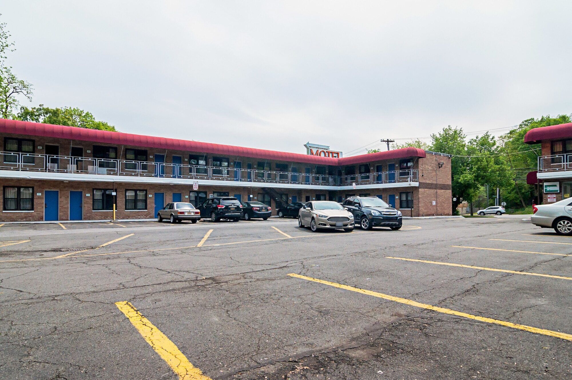 Een motel met een rood dak en meerdere verdiepingen, met een parkeerplaats met verschillende auto's.