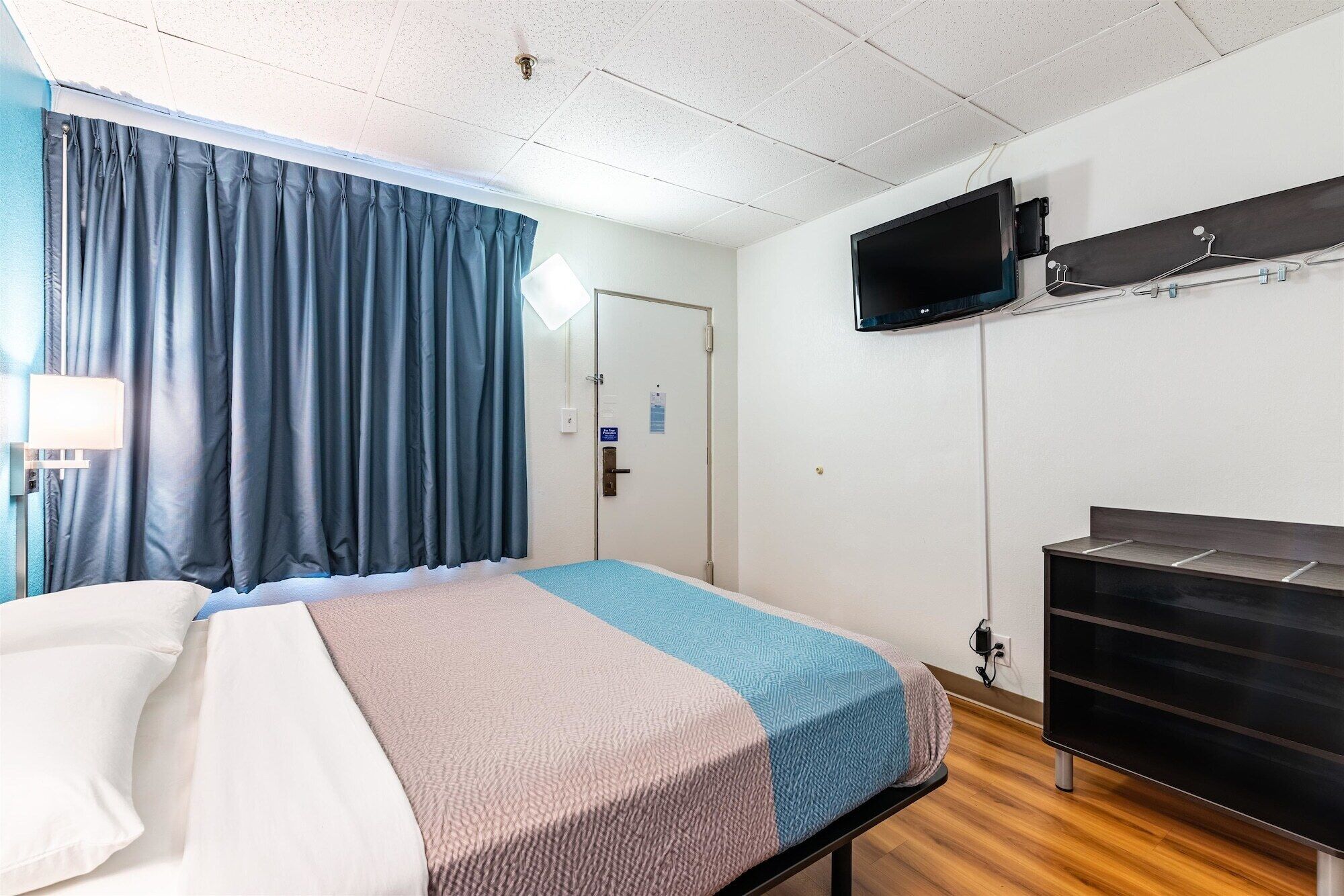 Une chambre d’hôtel avec un lit, un téléviseur fixé au mur, un bureau et une porte.