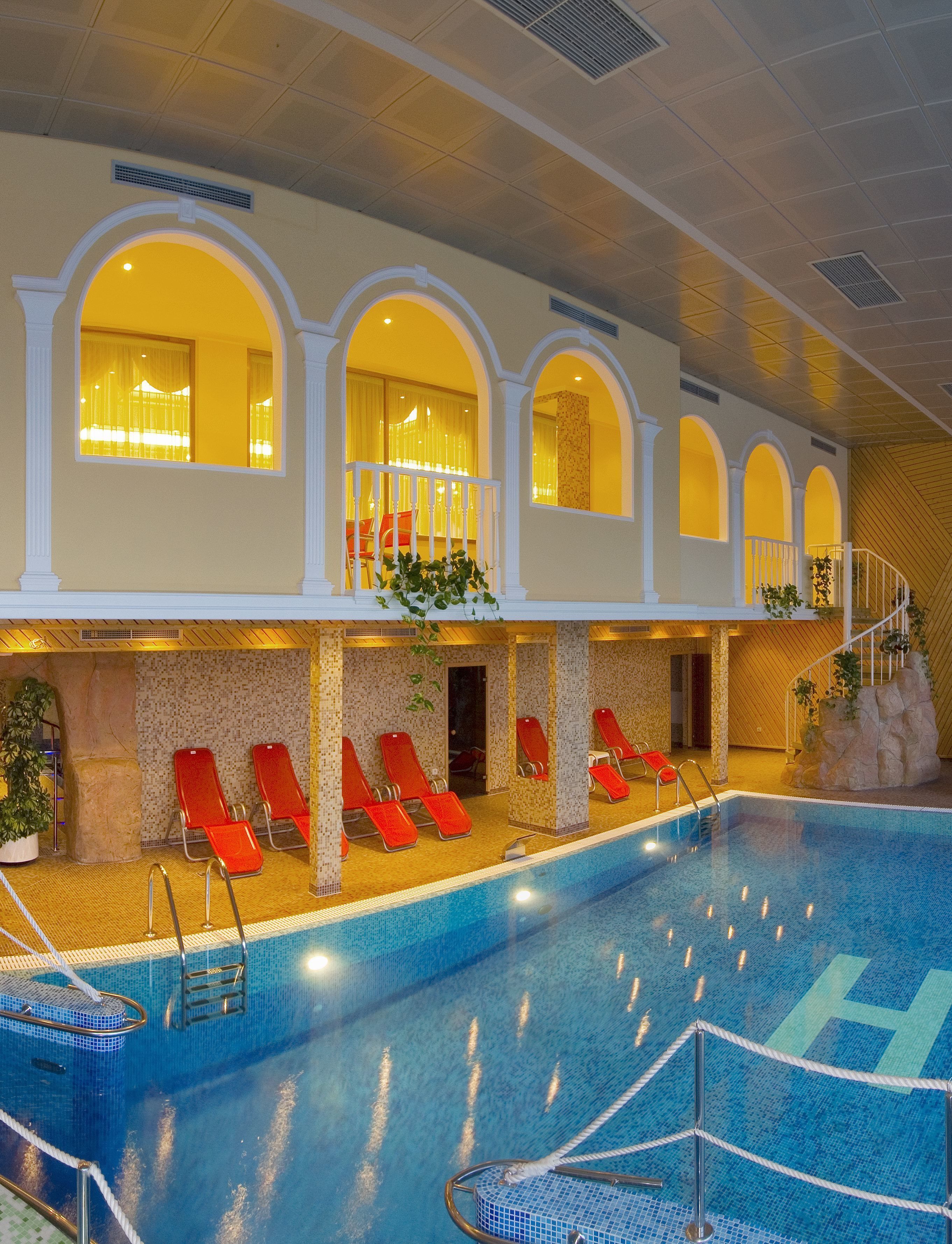 An indoor swimming pool with red lounge chairs, a staircase, and a view of the pool area.