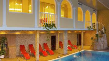 An indoor swimming pool with red lounge chairs, a staircase, and a view of the pool area.