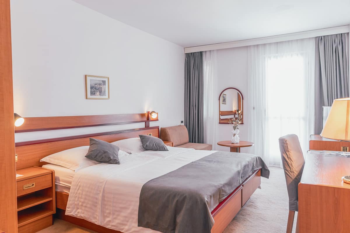 A hotel room with a bed, bedside table, chair, desk, lamp, and a mirror.