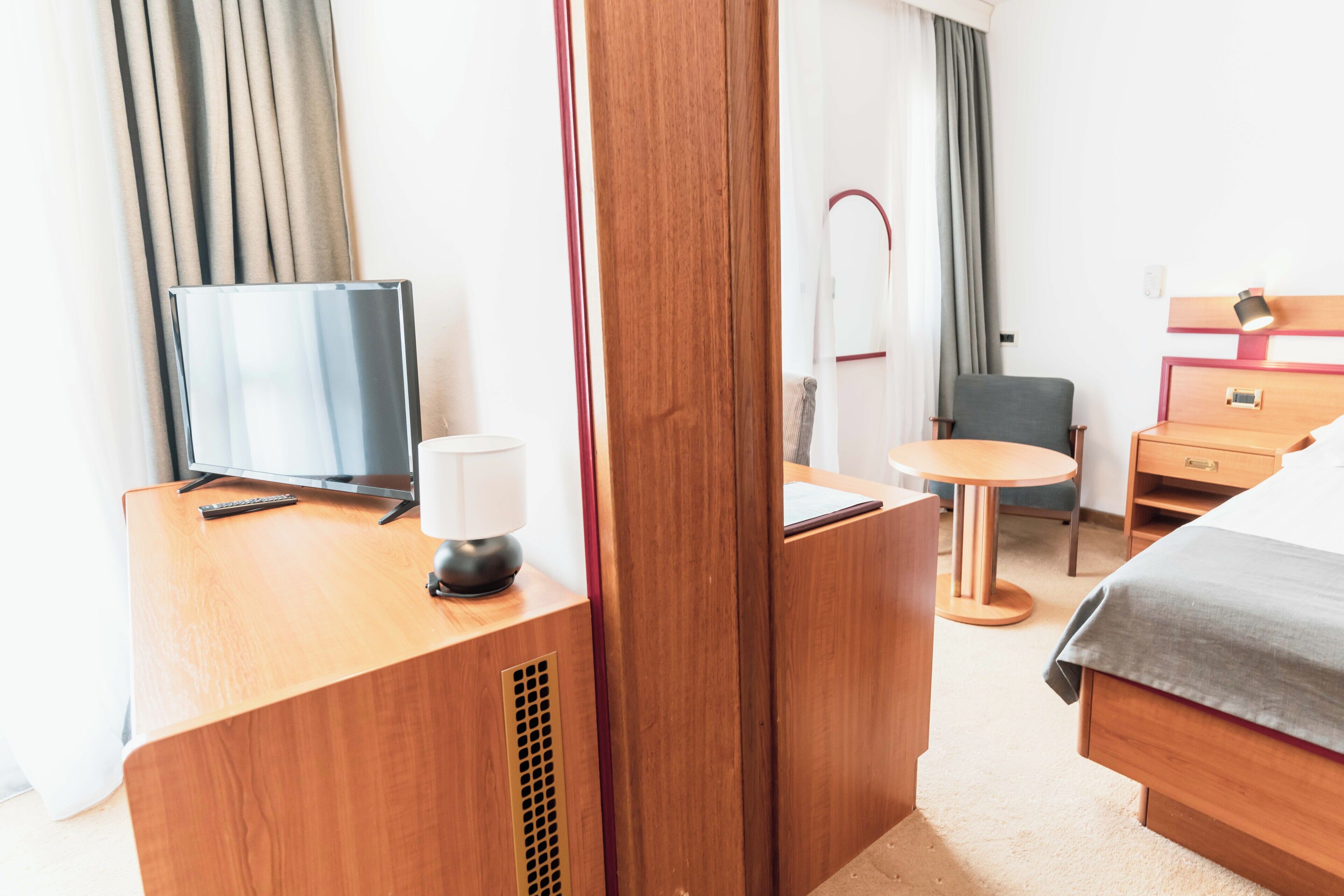 Ein Hotelzimmer mit Holzschreibtisch, Fernseher, Lampe, Stuhl, Bett und Nachttisch.